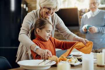 Happy little girl assisting her grandmother in setting the table for lunch at home.