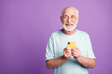 Sticker - Photo portrait of elderly man holding phone in two hands looking at blank space isolated on vivid purple colored background