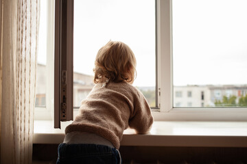 The child climbs to the window, the girl on the window sill rests on the net, the danger of falling. The child is alone at home, can fall out of the window.