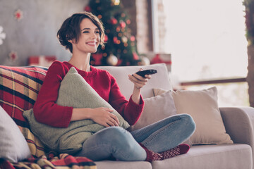 Sticker - Photo of cute cheerful young lady hold remote control embrace pillow sitting sofa wear red pullover jeans socks indoors