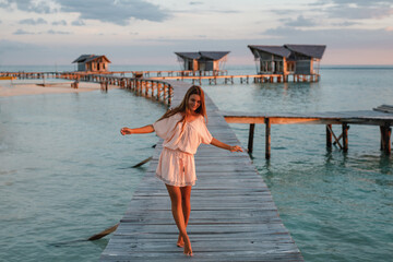 Wall Mural - Female tourist enjoying resort vacations in paradise nature environment, woman in stylish sundress walking at pier recreating during solo travelling for visiting  Maldive island