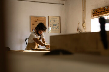 Hispanic man working as carpenter in a small wood laboratory. Bearded man concentrated on shaping a new piece of timber for a home furniture in his carpentry workshop. Entrepreneur people concept