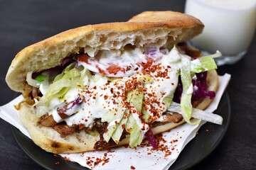 A delicious, fresh kebab from Germany lies on a wooden surface, next to it is an ayran and hot spice - a popular kebab to take away from Germany, the so-called Döner lies ready to eat at the table