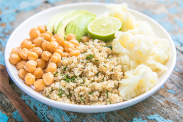 A bowl of healthy vegan and vegetarian lunch or dinner. Salad of fried chickpeas, quinoa, avocado, cauliflower on a light background.Top view, flat lay