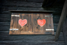 Close-up Of A Mountain Chalet With Wooden Window With Shutters And Two Painted Red Hearts, Italian Alps, Europe.