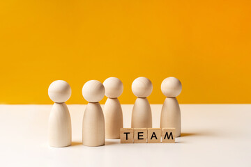 Company of wooden people on a yellow background with letters. The concept of team work and management, copy space