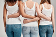 © Svitlana - Cropped shot of three diverse friendly women in white shirt and casual denim jeans putting arms around each other while standing together isolated over grey background