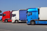 Fototapeta  - Various types and colors of cabins. Trucks parked in a row. Truck stop. Break in a trip.