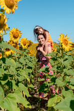 Smiling Mother Carrying Daughter On Shoulders In Sunflower Field
