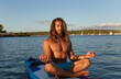 © Sus Pons/Westend61 - Young man with long hair meditating while sitting on paddleboard at sea against sky during sunset