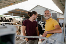 Smiling Mature Farmer With Adult Son At Cow House On A Farm