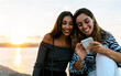 © Marco Govel/Westend61 - Young friends using phone while sitting on retaining wall at promenade during sunset