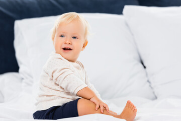 Selective focus of cheerful toddler boy looking at camera on bed