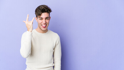 Wall Mural - Young caucasian man isolated on purple background showing rock gesture with fingers