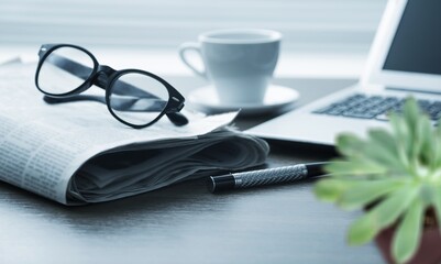 Fresh newspaper with laptop computer and glasses on table