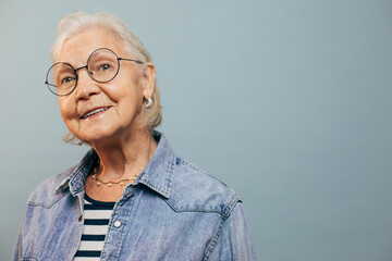Interested confident elderly woman with short white hair and gray eyes in stylish wear looking away and thinking about something good. Isolated over light studio background.