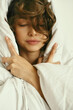 © Дарья Чачева - Portrait of young beautiful girl with blanket on white background. At home. Comfort. Healthy lifestyle, clear skin. Curly hair. Emotions. About sleeping and awakening.