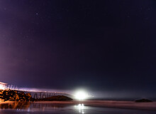 Richfield Pier Reflects In The Wet Sand Of Mussel Shoals Beach With Constellation Stars In Sky Above.