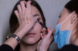 © OliaVesna - the process of applying makeup to a beautiful brunette by a master in a medical mask. beauty, modeling and cosmetics concept.