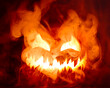 © Leigh Prather - Fiery red hot Halloween jack o lantern pumpkin carved with scary evil face glowing brightly with thick smoke.