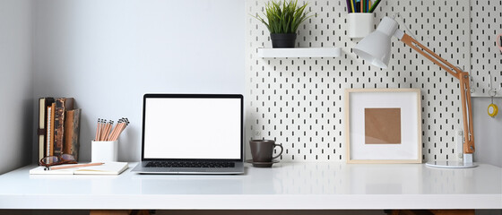 Mockup blank screen laptop and office supplies on white desk.