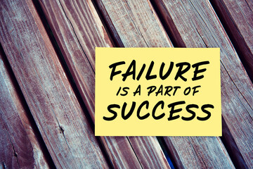 Wall Mural - Failure is a part of success inspirational motivational quote written on yellow paper on a wooden table.