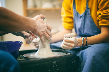 Woman learning to make ceramic utensils in a workshop at a lesson with a teacher on a potter's wheel, hands in clay close-up