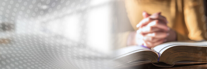 woman praying with her hands over the bible, hard light; panoramic banner