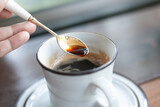 Fototapeta Sawanna - A hand holding siver spoon scooping some hot black coffee from a white ceramic mug