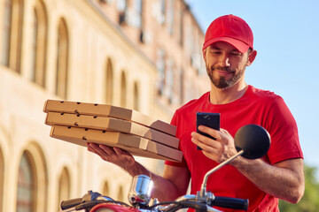 Smiling caucasian male courier with smartphone and pizza