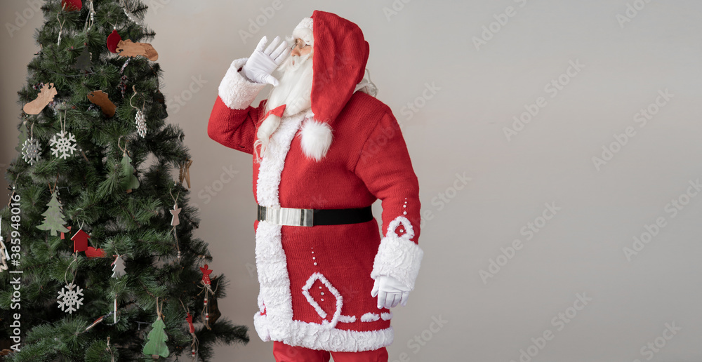 santa claus dressed in a red suit stands near the christmas tree. He ...