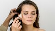 © markwar - Attractive female face of a brunette well-groomed woman. Master applies makeup with a big fluffy brush in a beauty salon. Beauty industry of cosmetics backstage of professional makeup.