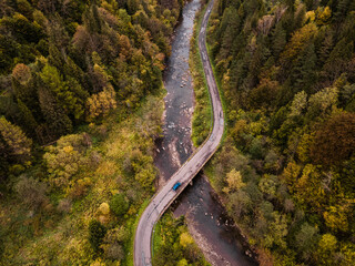 Wall Mural - Blue Car Crossing River on Bridge in Forest on Winding Curvy Road. Road Trip Outdoor Adventure in Wilderness. Drone View