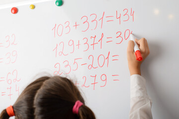 Young primary school pupil calculating mathematical equations on the white board during a math class. Education, learning math concept.
