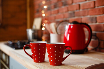 Kitchen in loft style with red accents. Red cups and electric kettle in loft kitchen on background of brick wall. Cozy home. 