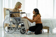 © ake - caucasian senior patient recover woman on wheelchair and mixed race daughter in hospital room new normal.