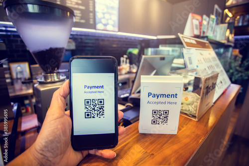 Customer hand using smart phone to scan Qr code payment tag  with blurry coffee grinder and cashier machine in coffee shop to accepted generate digital pay without money. Qr code payment concept.
