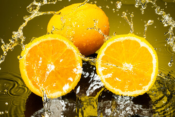 two oranges, whole and cut in half with drops and splashes of water on dark glass with gradient background and reflection