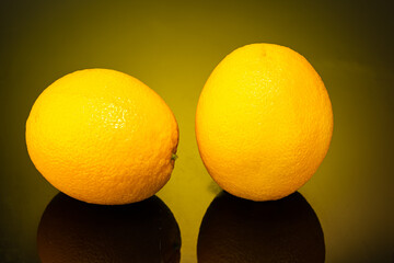 two oranges, whole and in slices on dark glass with a gradient background and reflection