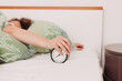 © Robert Petrovic - Tired woman in bed reaching out for analogue alarm clock to turn it off at 7 am, close up shot.