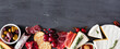 Assortment of cheese and meat appetizers. Top view bottom border on a slate stone banner background with copy space.