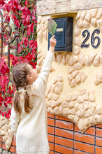 Little Girl In A White Knitted Dress Putting A Grape Leaf In The Mailbox In An Autumn Park In The Evening.