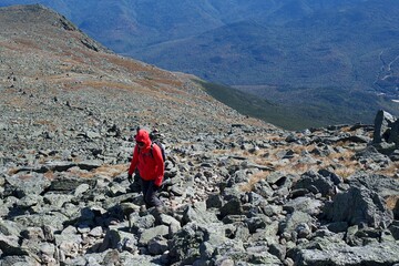 lone hiker trekking to the summit of mount washington over a rocky terrain in cold windy weather