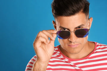 Wall Mural - Handsome man wearing sunglasses on blue background, closeup