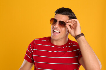 Wall Mural - Handsome man wearing sunglasses on yellow background