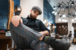 Stylishly dressed barber sits on chair in the salon