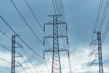 Wall Mural - High voltage electric pylon and electrical wire against blue sky and clouds. Bottom view of electric pylon. High voltage grid tower with wire cable. Transmission lines on high voltage grid tower.