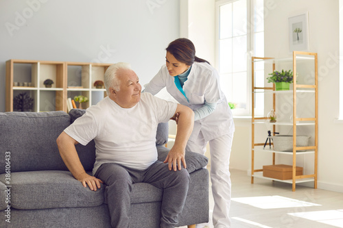 Nurse helping senior man to stand up from sofa in modern hospital or geriatric rehabilitation center