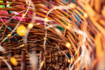 A blurry background of small yellow lanterns on a thin garland burns with a gentle light in a wicker brown wooden basket made of vines. Magical fairy-tale holiday or Christmas