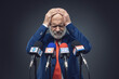 © stokkete - Sad politician with head in hands at the media briefing